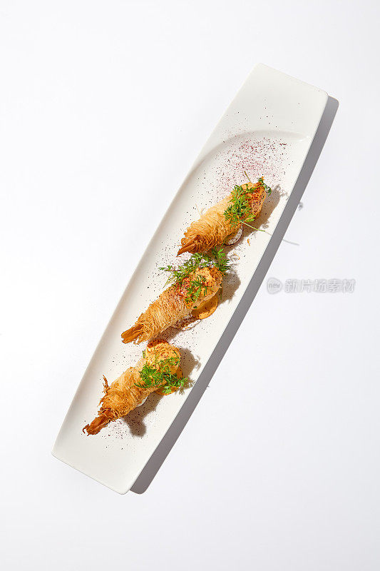 传统的希腊开胃菜- kataifi裹虾放在白色盘子里。夏日的kataifi酥皮虾。虾开胃菜，在kataifi面团里炸。现代风格的脆虾。